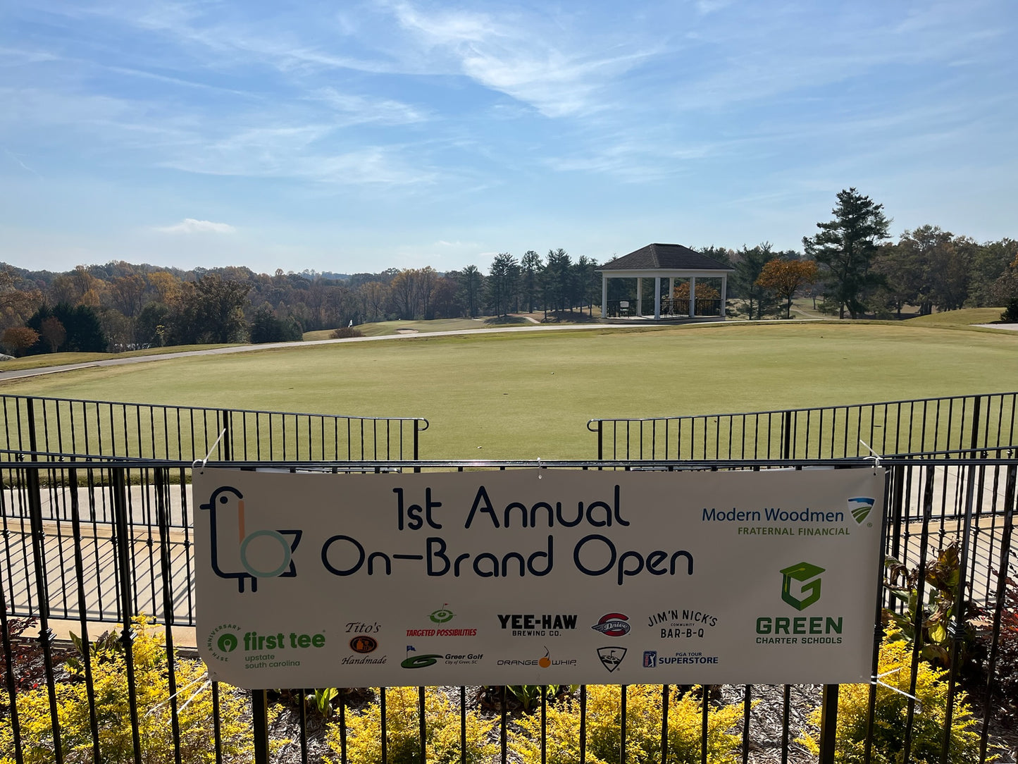 Golf course with a sign for the '1st Annual On-Brand Open' event, featuring multiple sponsors.
