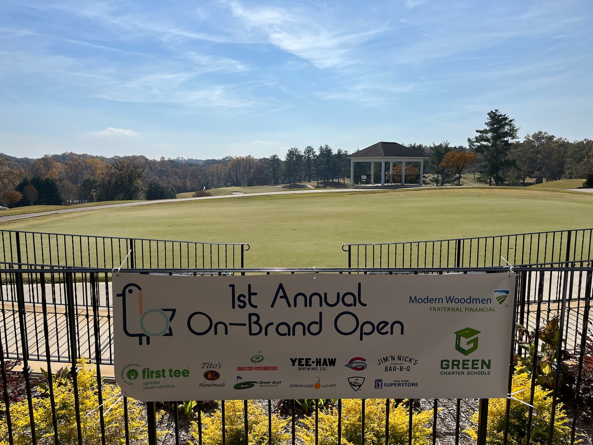 Golf course with a sign for the '1st Annual On-Brand Open' event, featuring multiple sponsors.