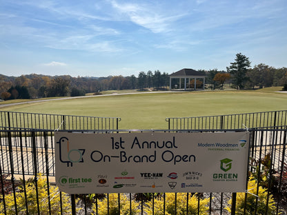 Golf course with a sign for the '1st Annual On-Brand Open' event, featuring multiple sponsors.