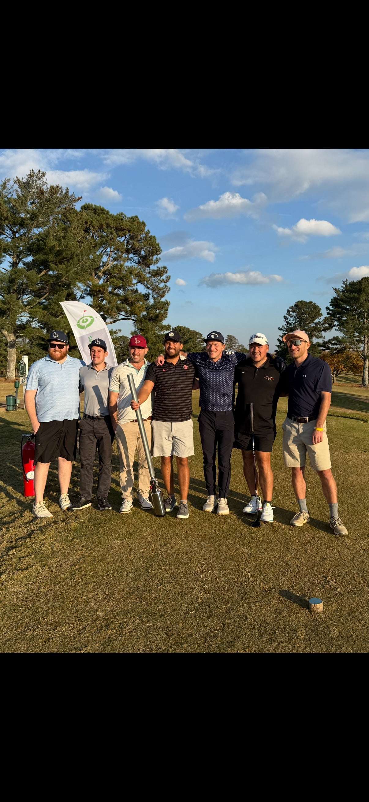Group of golfers at On-Brand tournament posing on a golf course with a clear sky.