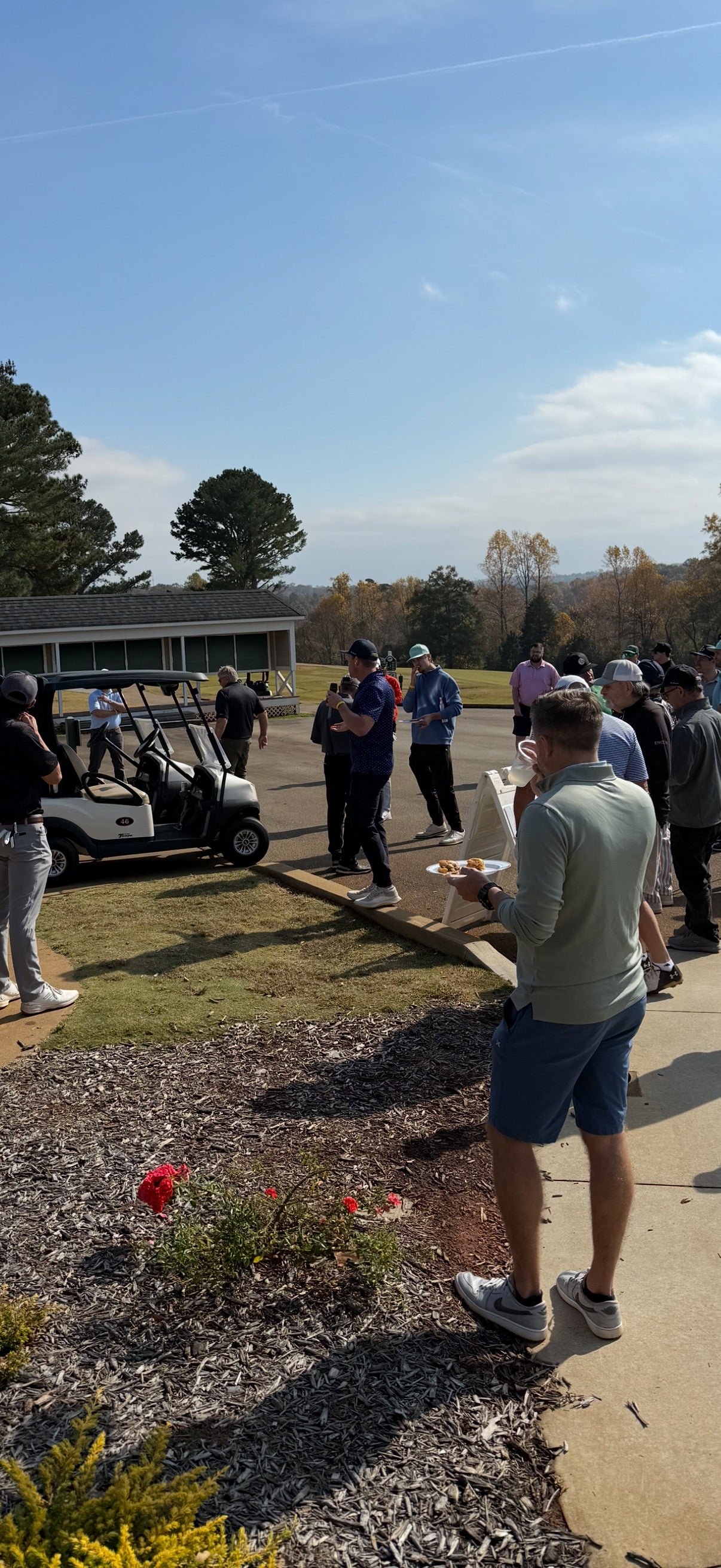 Group of people standing outdoors with golf carts and a clear sky at On-Brand Open charity golf tournament