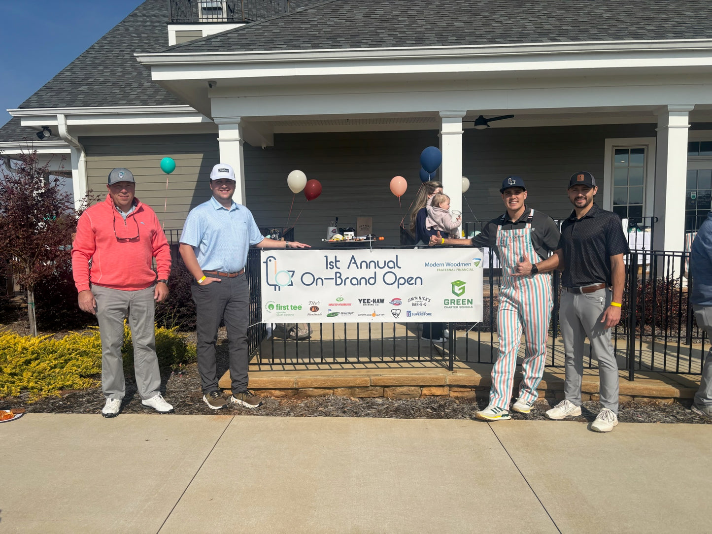 Group of golfers standing in front of a golf course with a banner for the '1st Annual On-Brand Open'.