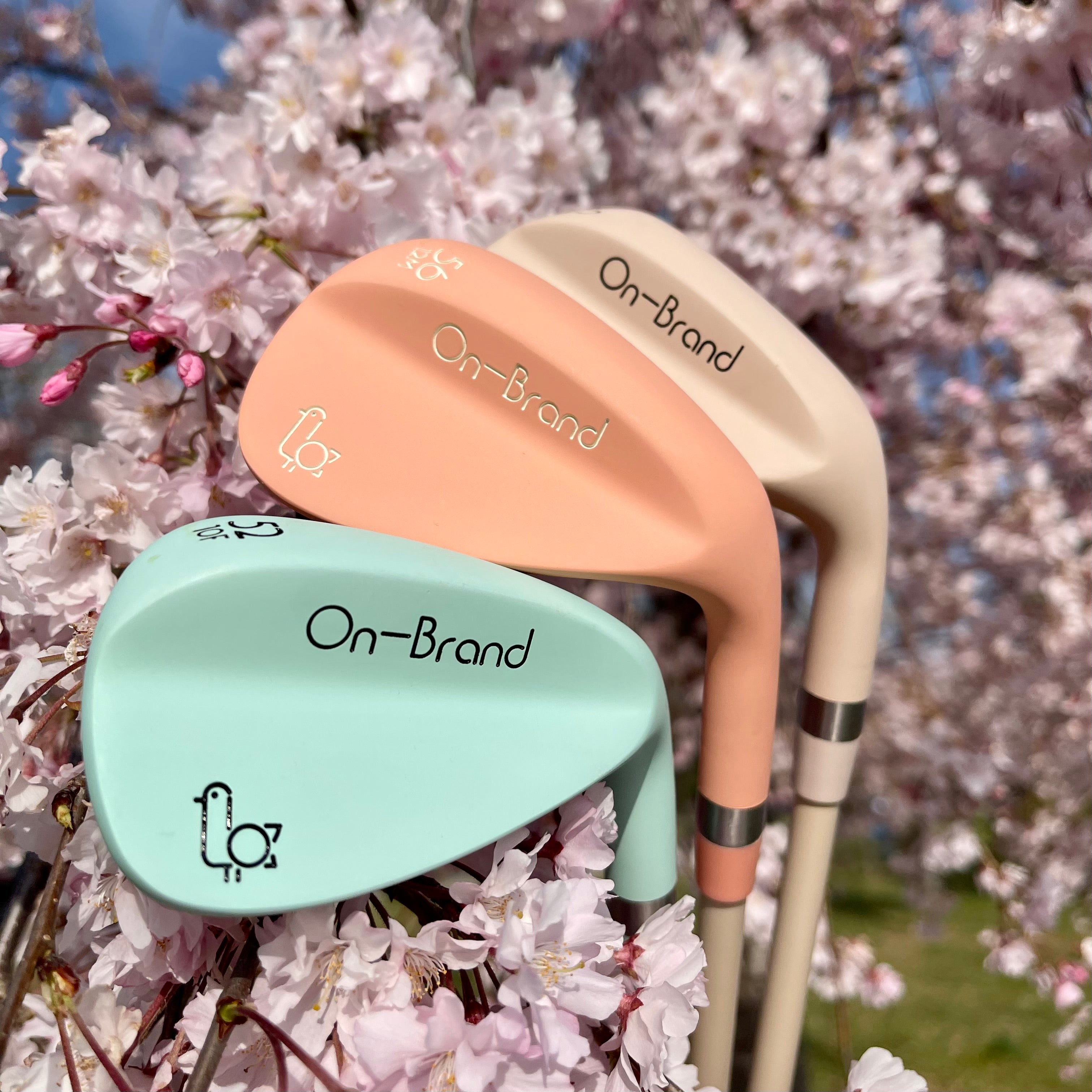 Two golf clubs, one peach and one green, with 'On-Brand' text against a cherry blossom background.