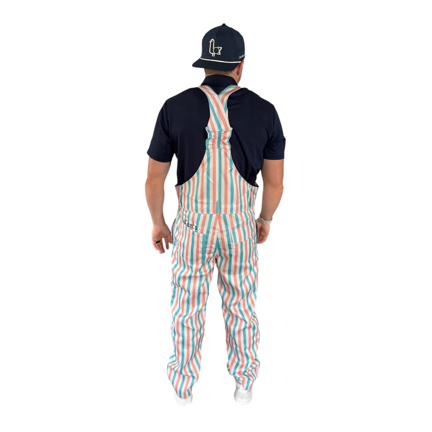 Back view of On-Brand Golf Pair-a-Keets striped bib overalls worn with a navy polo and seagull cap