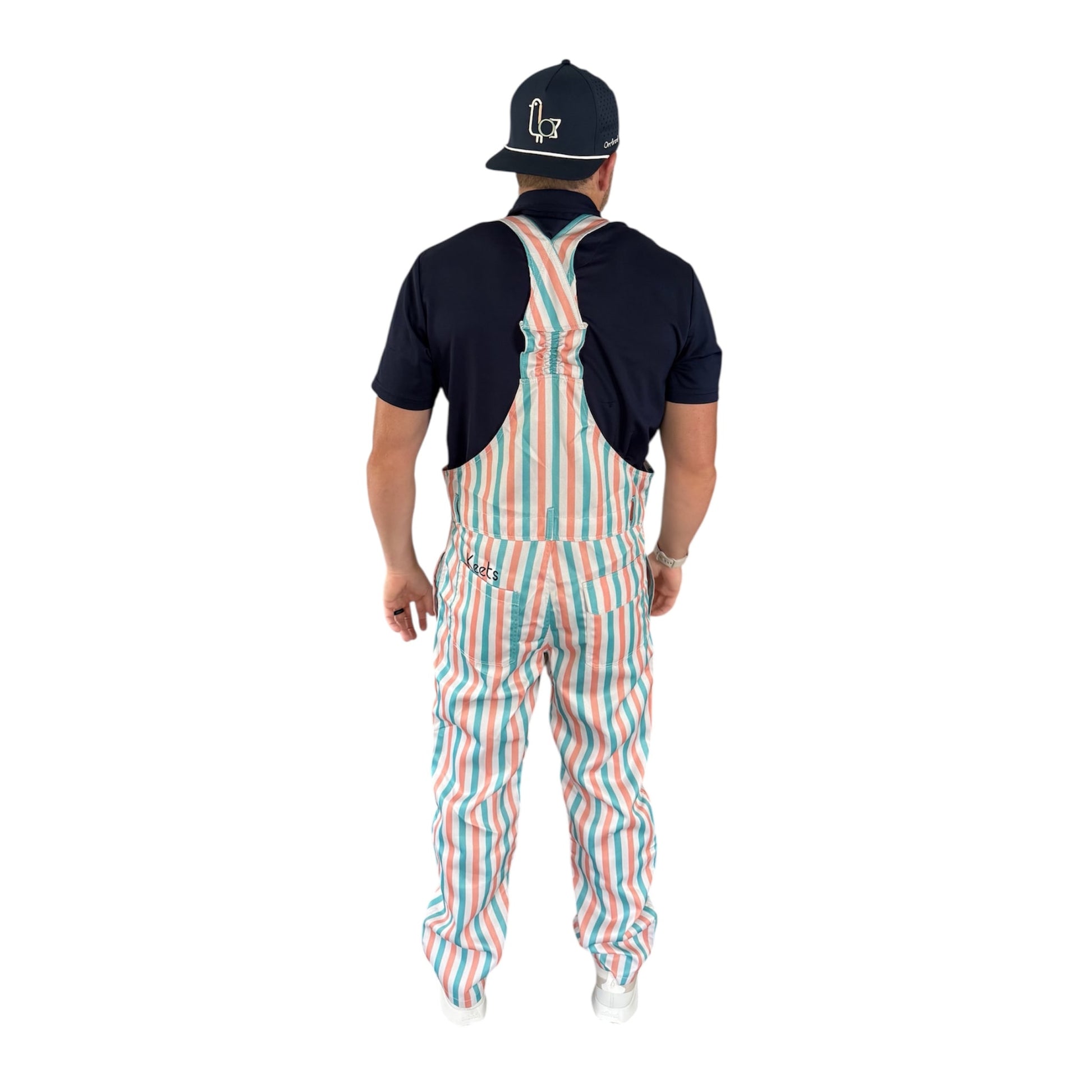 Back view of On-Brand Golf Pair-a-Keets striped bib overalls worn with a navy polo and seagull cap