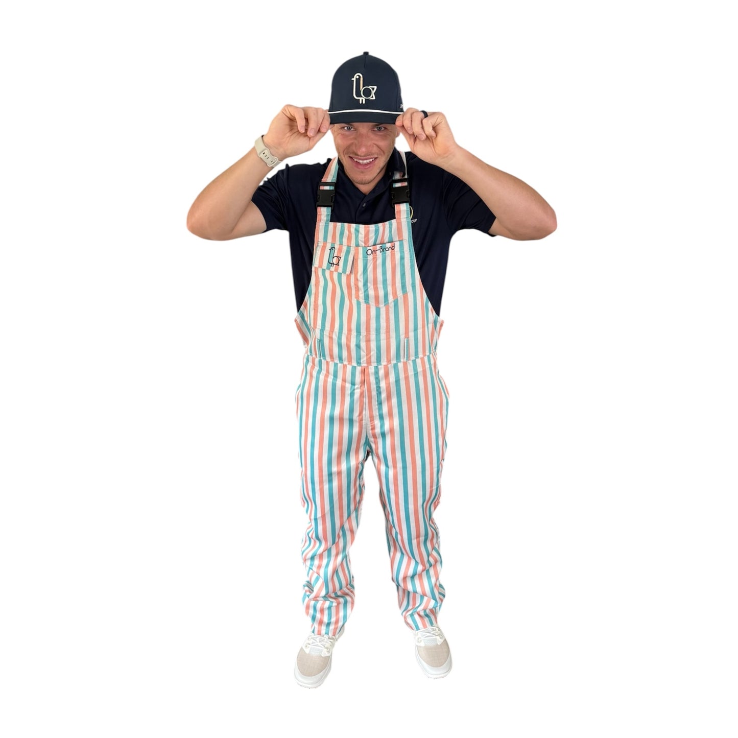 Golfer in On-Brand Golf Pair-a-Keets peach, seafoam, and cream striped bib overalls tipping a navy seagull cap, front view