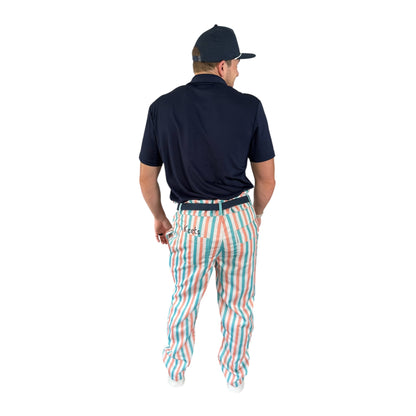 Back view of On-Brand Golf Pair-a-Keets pastel-striped golf trousers worn with a navy polo and seagull cap