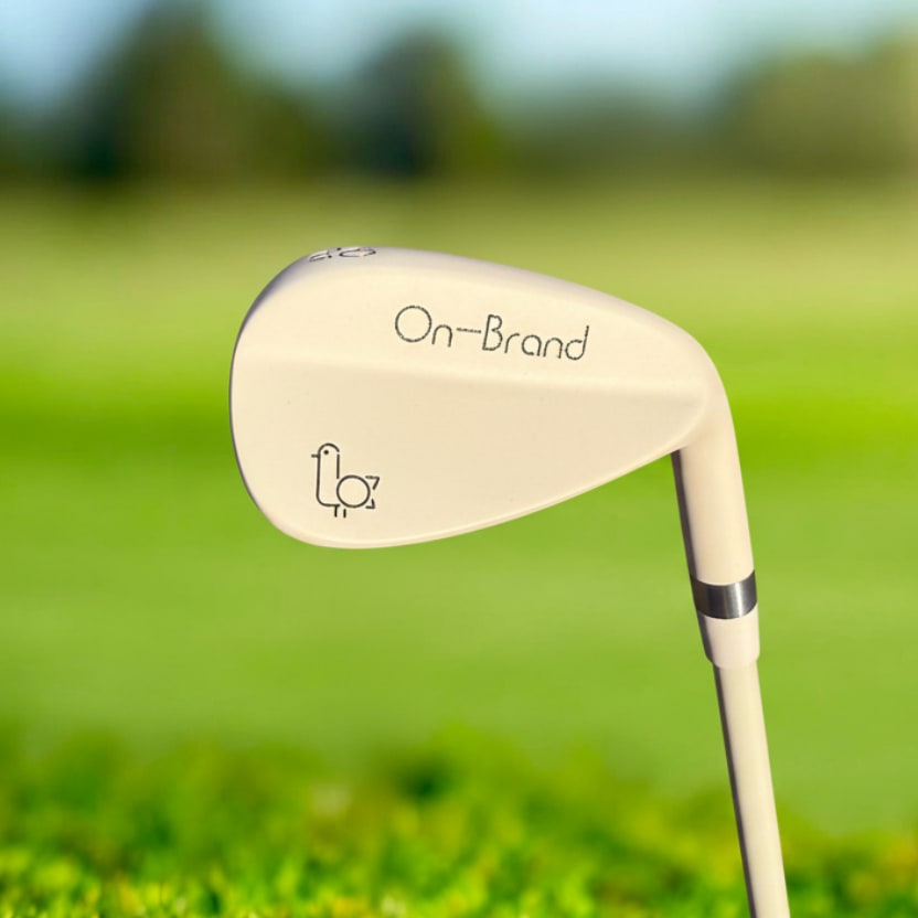 Cream Phoenix Wedge by On-Brand Golf photographed on a golf course with the fairway in the background