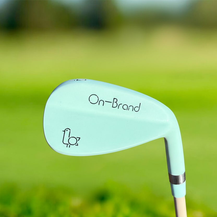 Seafoam Phoenix Wedge by On-Brand Golf photographed on a golf course with the fairway in the background