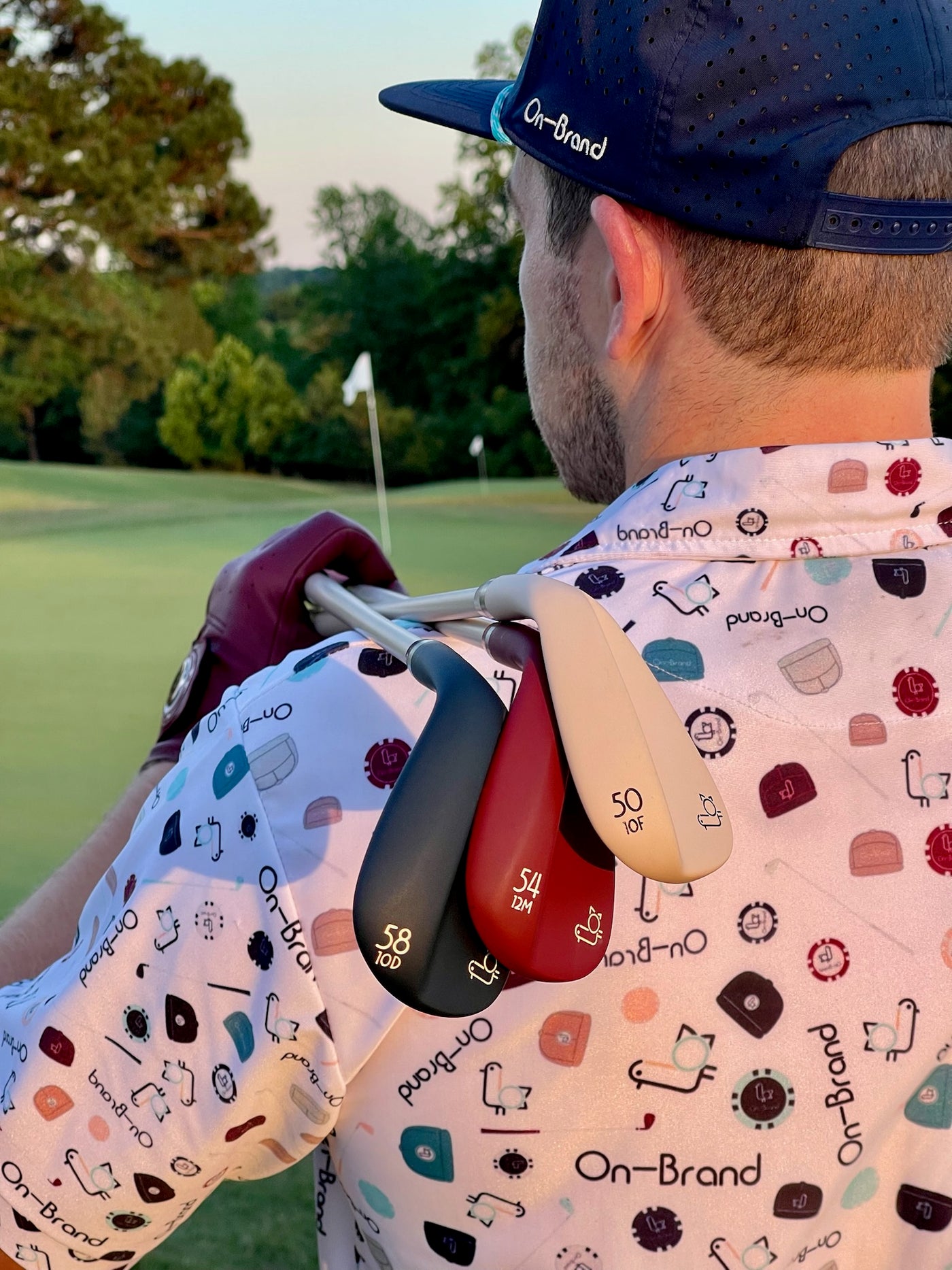 Navy, burgundy, and cream Phoenix Wedges resting on a golfer's shoulder on the course at sunset – On-Brand Golf